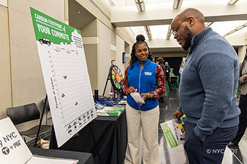 Two individuals, engaged in conversation, stand beside a table featuring a sign and educational materials